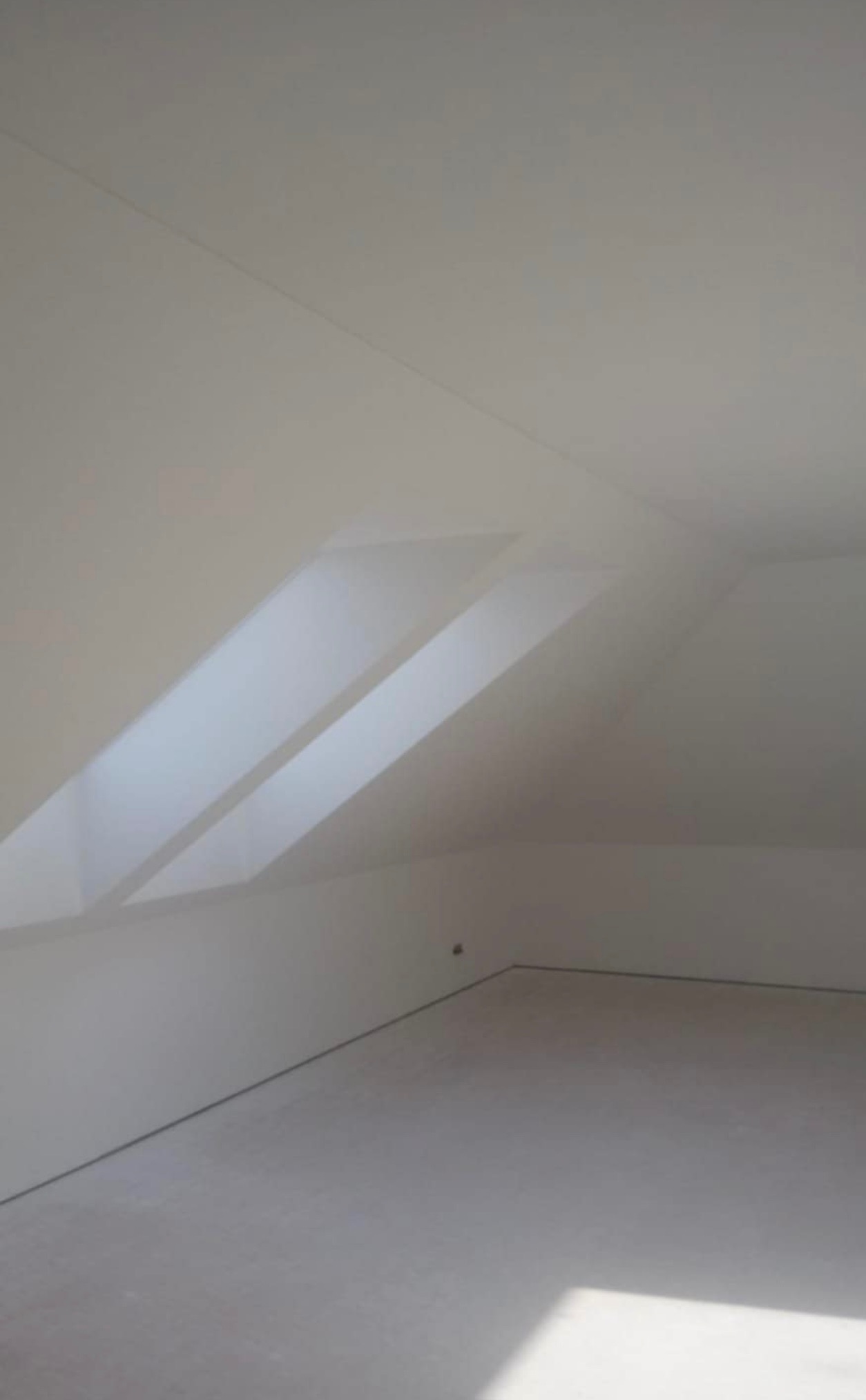 Poddasze po remoncie z dwoma oknami dachowymi, ściany i podłoga w jasnym odcieniu szarości, widoczne łączenia płyt karton gips na suficie.