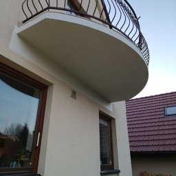 Al'kinshpul SERHII TYKHONENKO - Elewacja budynku z półokrągłym balkonem z ozdobną, metalową balustradą. Widoczne okna z brązowymi ramami i fragment dachu sąsiedniego budynku.