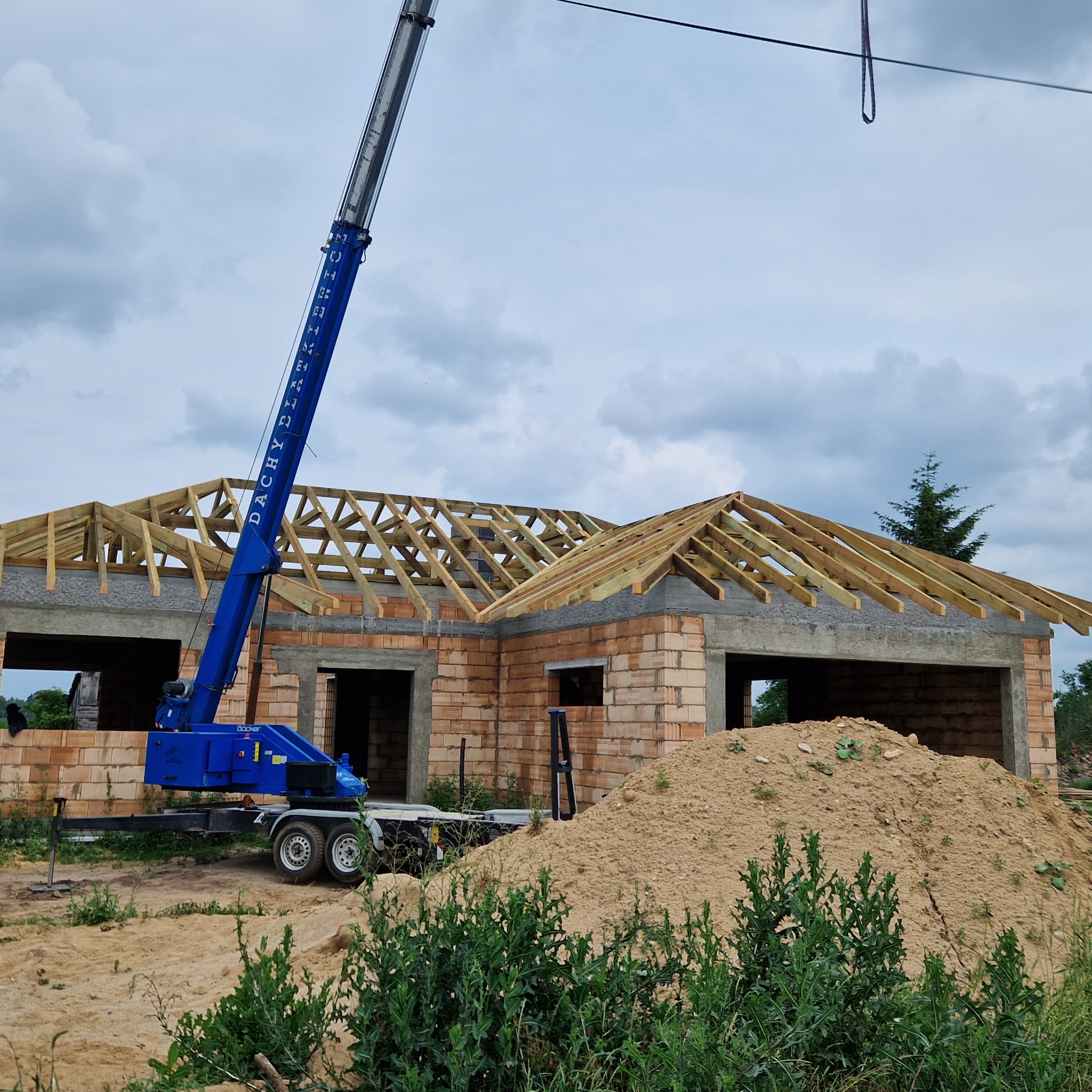 Budowa domu jednorodzinnego w trakcie montażu drewnianej konstrukcji dachu z użyciem dźwigu.