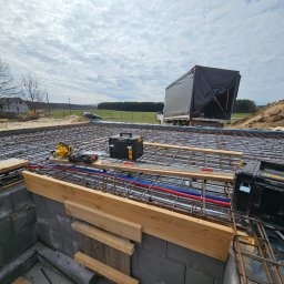 Prowood Sławomir Szczukowski - Zbrojenie płyty fundamentowej z instalacją podposadzkową (rury CO i wod-kan) na budowie domu jednorodzinnego. Widoczne narzędzia i skrzynki narzędziowe.