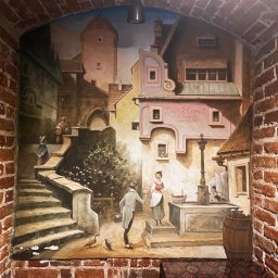 Tigran Vardikyan - Malowidło ścienne w ceglanej arkadzie, ukazujące historyczną uliczkę z kamienicami, schodami, postaciami przy studni i szyldem 'Beer Street SINCE 1829'.
