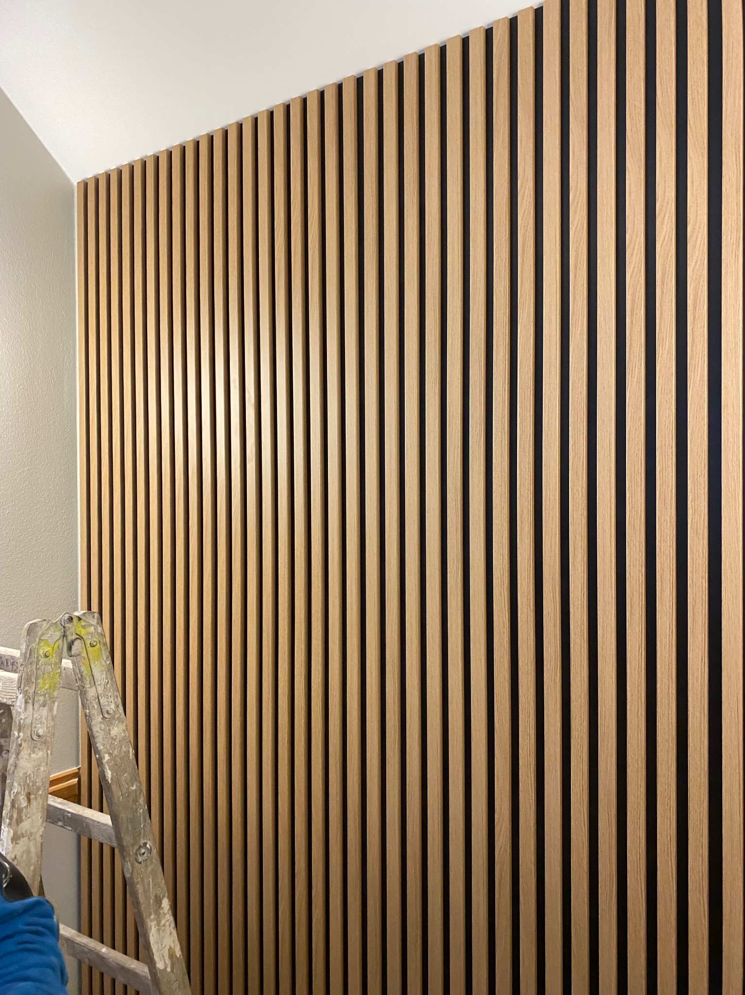 Drewniane lamele na ścianie w pionowym układzie, widoczna drabina malarska. Wykończenie wnętrza z elementami dekoracyjnymi, nowoczesny design.