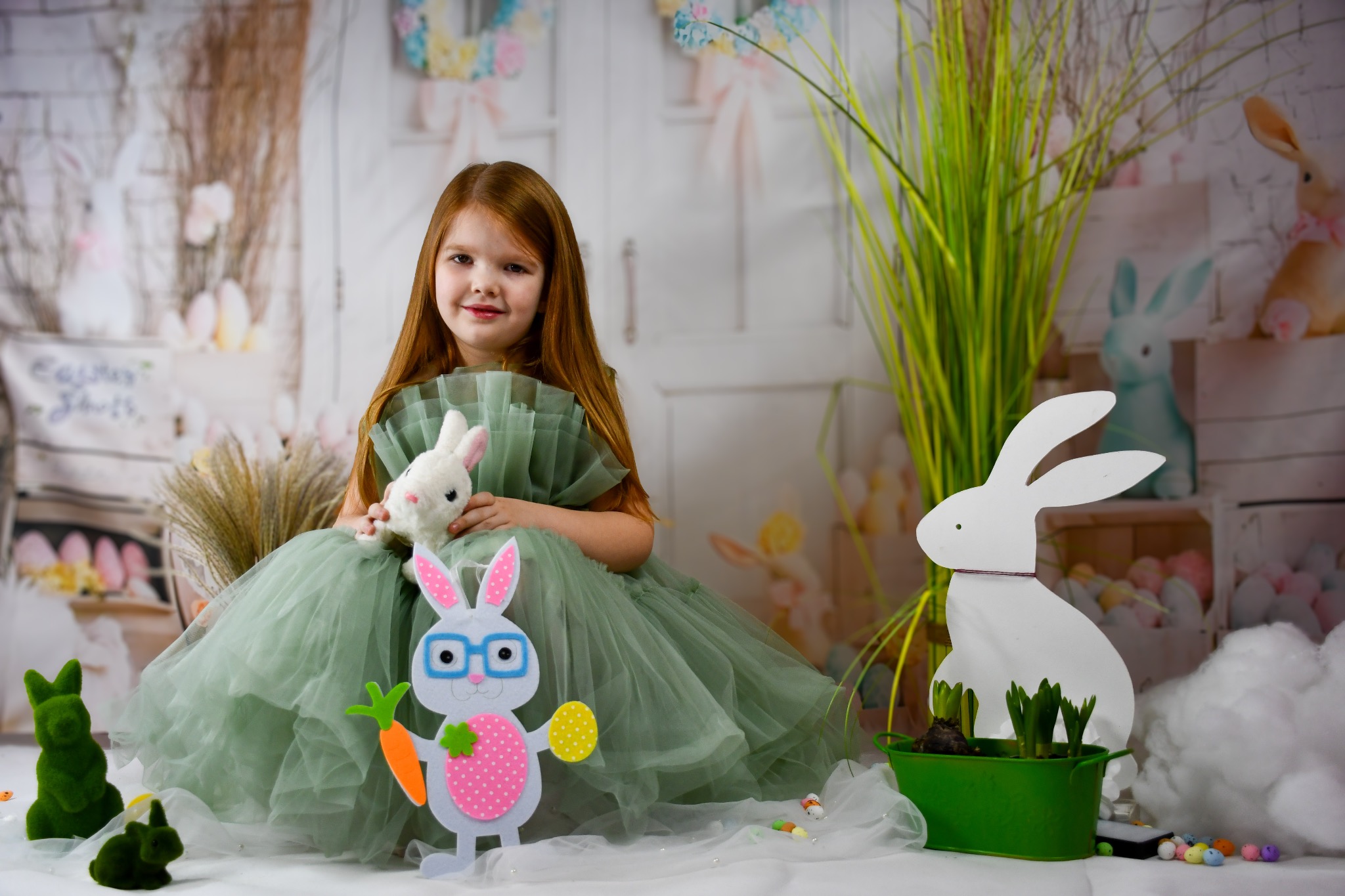 Dziewczynka w tiulowej sukience pozuje z pluszowym króliczkiem w scenerii wielkanocnej w Ostrówku, z dekoracjami królików i jajek w pastelowych kolorach.
