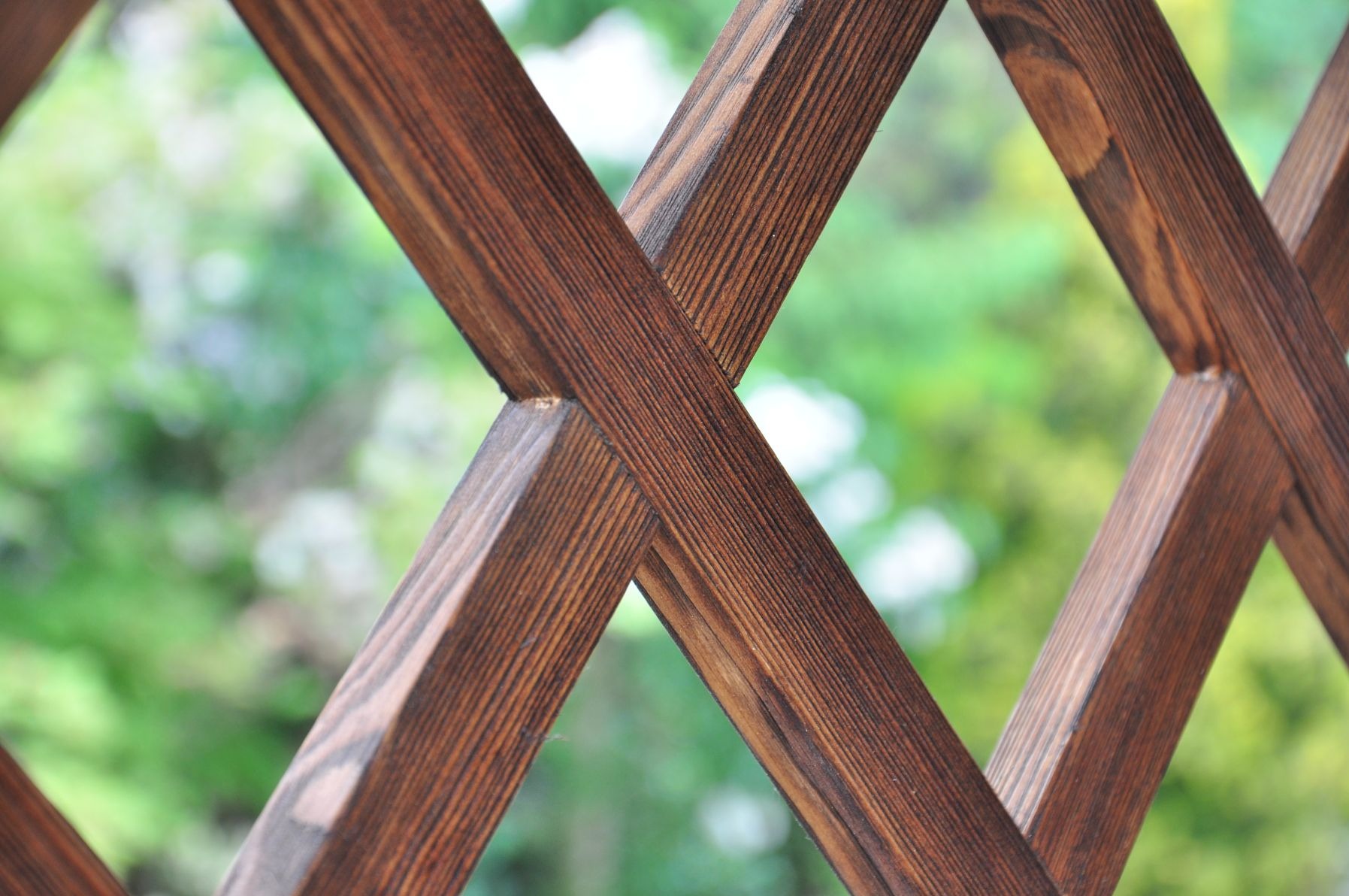 Drewniana konstrukcja kratowa z ciemnobrązowego drewna na tle rozmytej zieleni ogrodu.