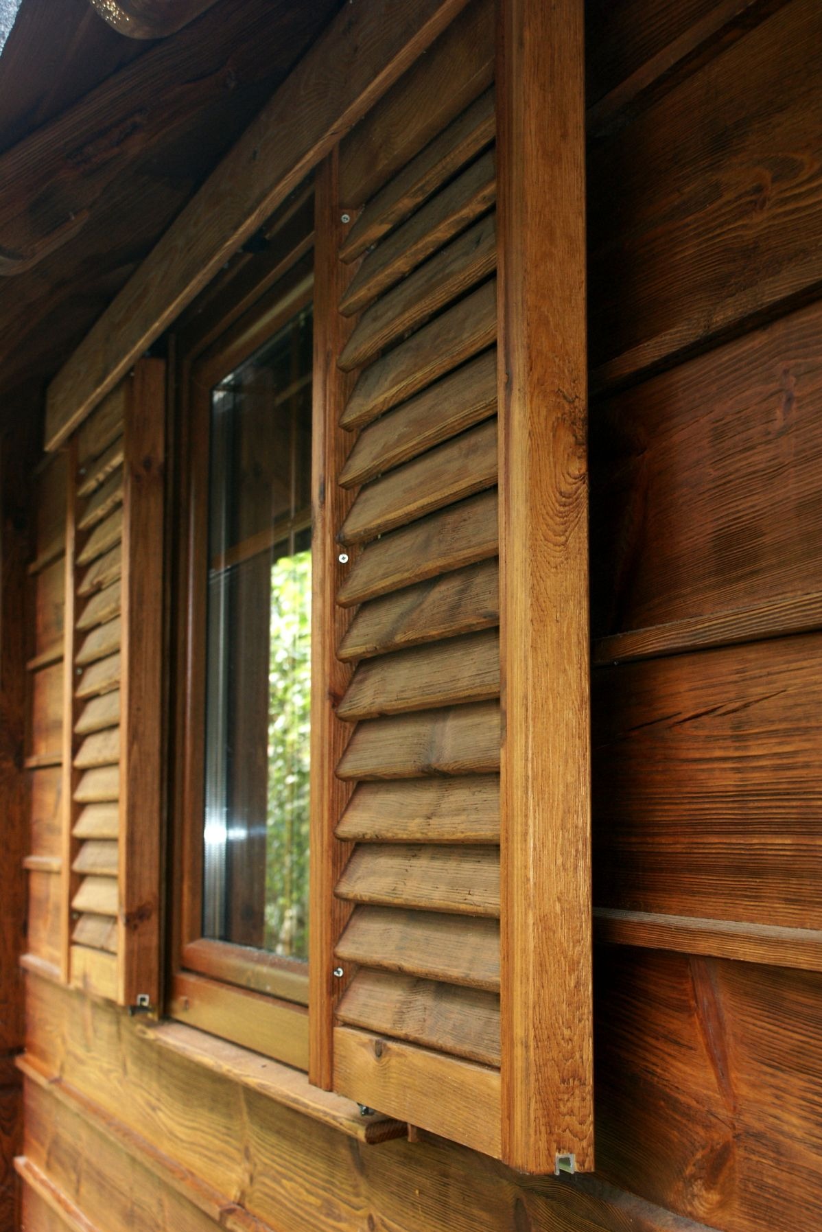 Drewniane okiennice z żaluzjami zamontowane na budynku z desek, widoczne mocowania i faktura drewna.