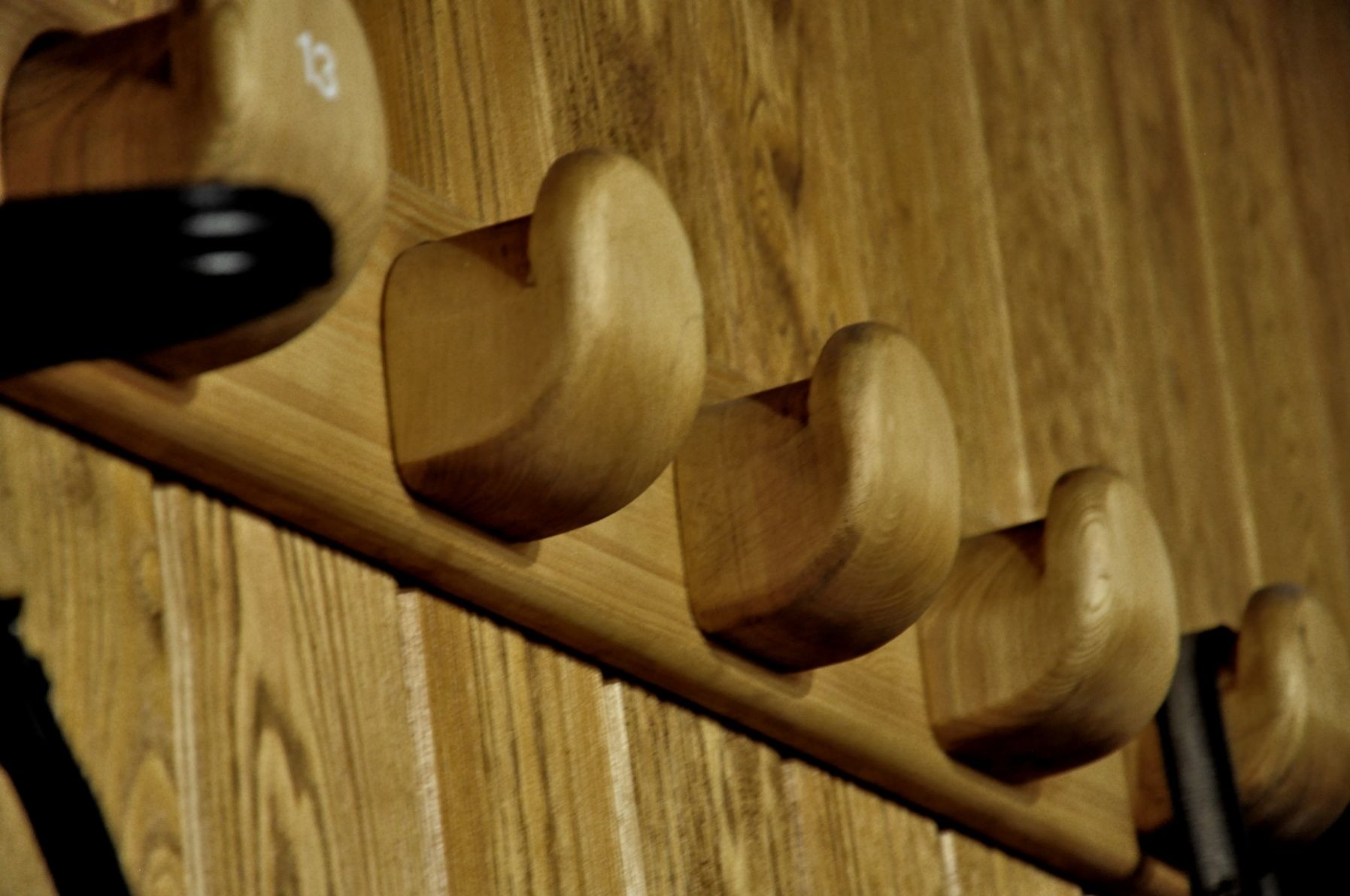 Drewniany wieszak ścienny z czterema uchwytami w kształcie zaokrąglonych kostek, jeden z uchwytów z czarnym elementem, całość zamontowana na panelu z jasnego drewna.