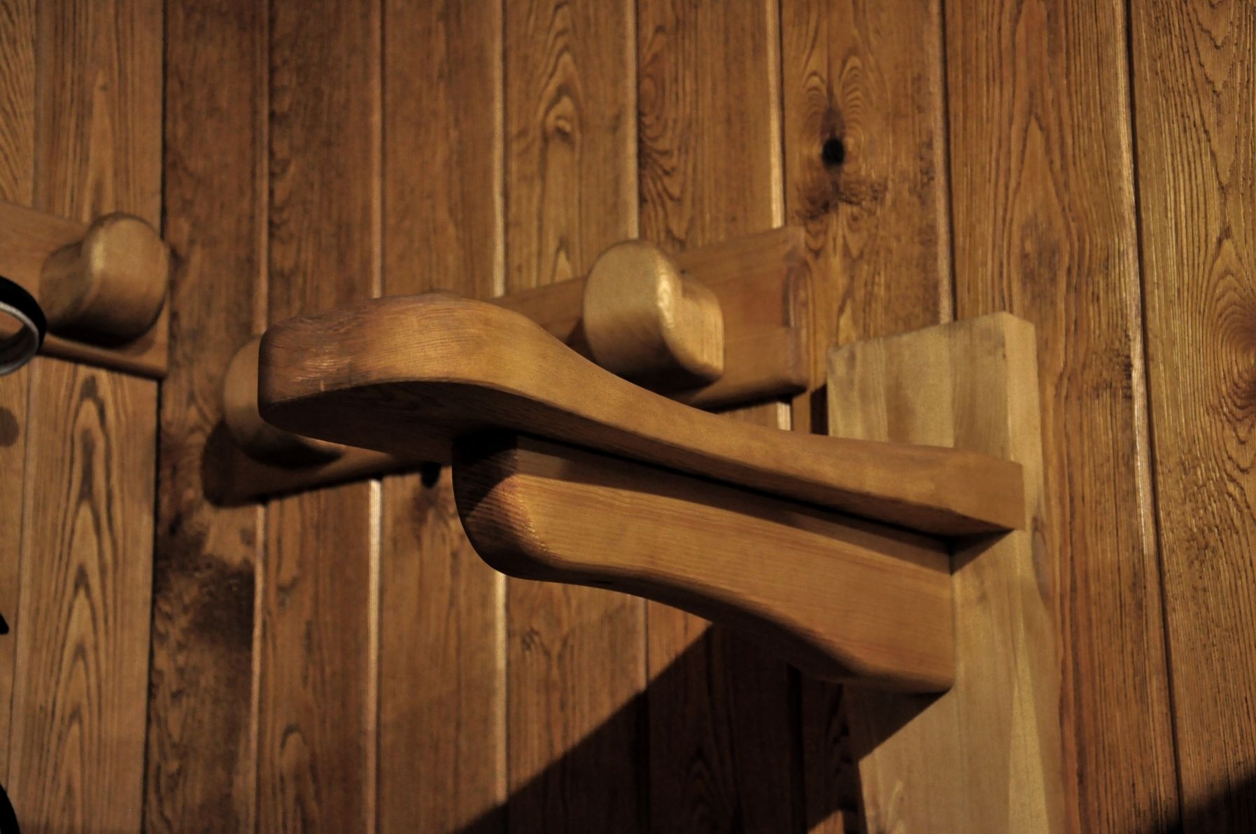 Fragment drewnianej konstrukcji z zaokrąglonymi elementami, przymocowanej do boazerii w ciepłym oświetleniu.