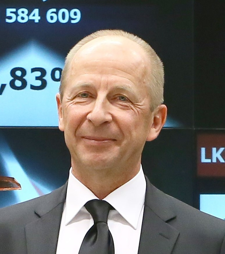 Portret uśmiechniętego mężczyzny w garniturze na tle ekranu z danymi finansowymi. Profesjonalizm i zaufanie w doradztwie biznesowym.