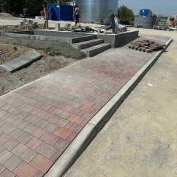 STATUS-BRUK Petro Tsymbaliak - Układanie kostki brukowej: ścieżka z kostki w odcieniach czerwieni i brązu, obrzeża betonowe, schody z kostki, elementy przygotowane do ułożenia, teren budowy.