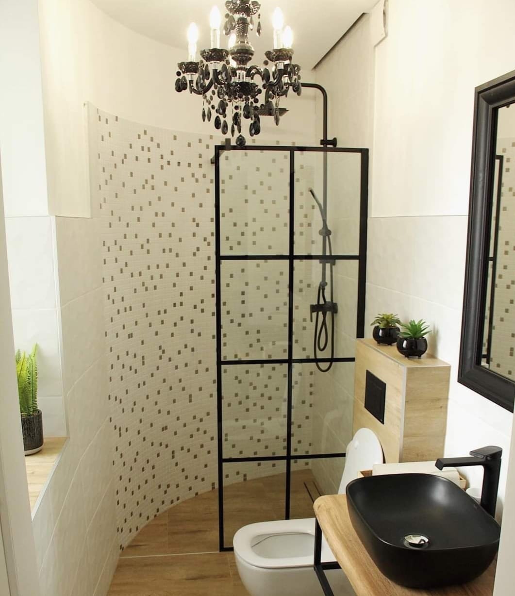 Nowoczesna łazienka z kabiną prysznicową typu walk-in z czarną ramą, armaturą w kolorze czarnym, umywalką nablatową w kształcie misy i dekoracyjnym żyrandolem.