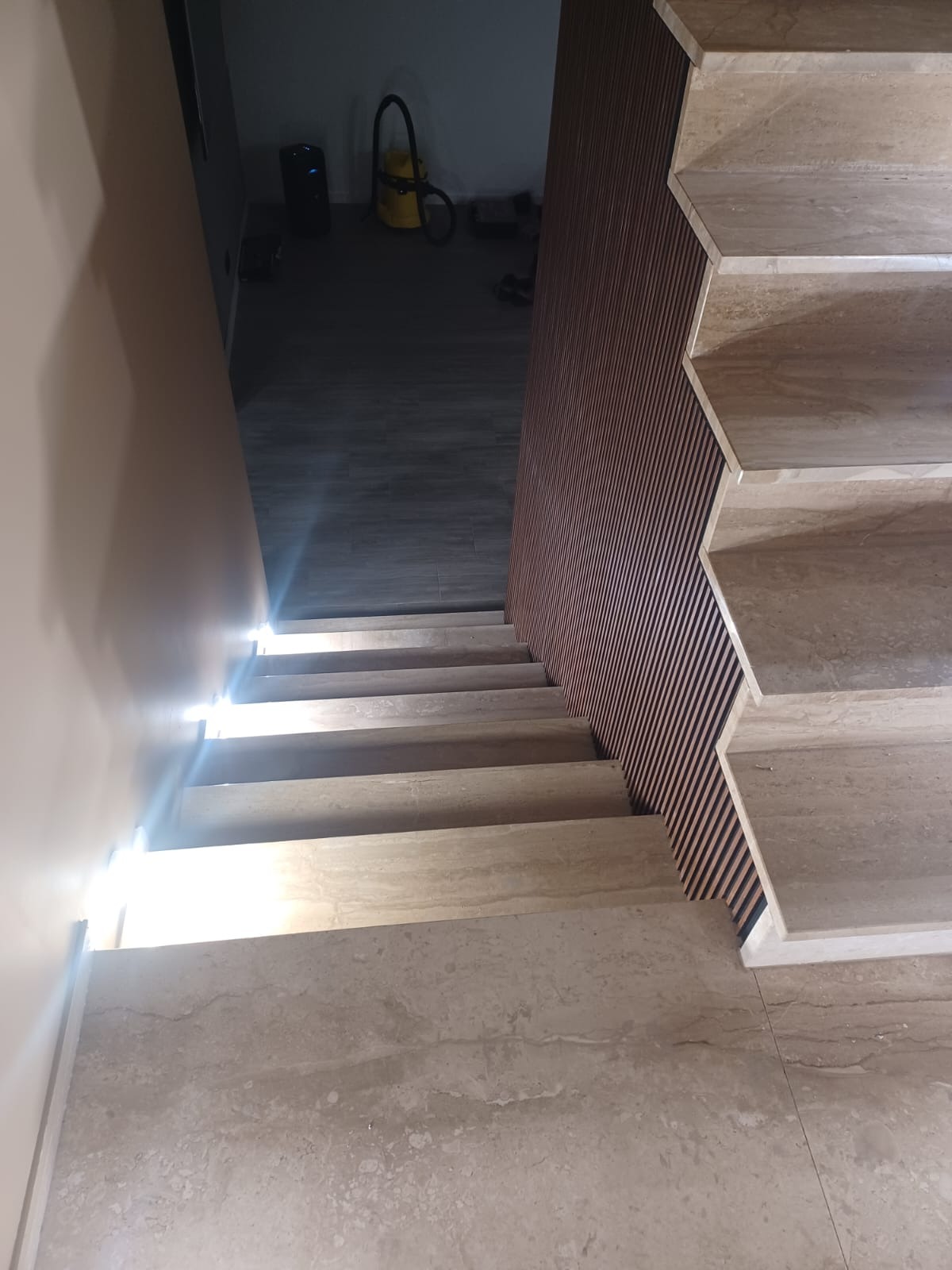 Marmurowe schody z podświetleniem LED, widok z góry, obok drewniana ściana z listewek, w tle odkurzacz przemysłowy.