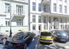 Elewacja kamienicy z balkonem, widok z ulicy z zaparkowanymi samochodami, tabliczka z numerem na budynku.