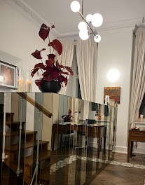 Eleganckie wnętrze kancelarii z lustrzaną balustradą schodów, ciemnoczerwony anturium w czarnej donicy, nowoczesna lampa sufitowa i drewniane biurko w tle.