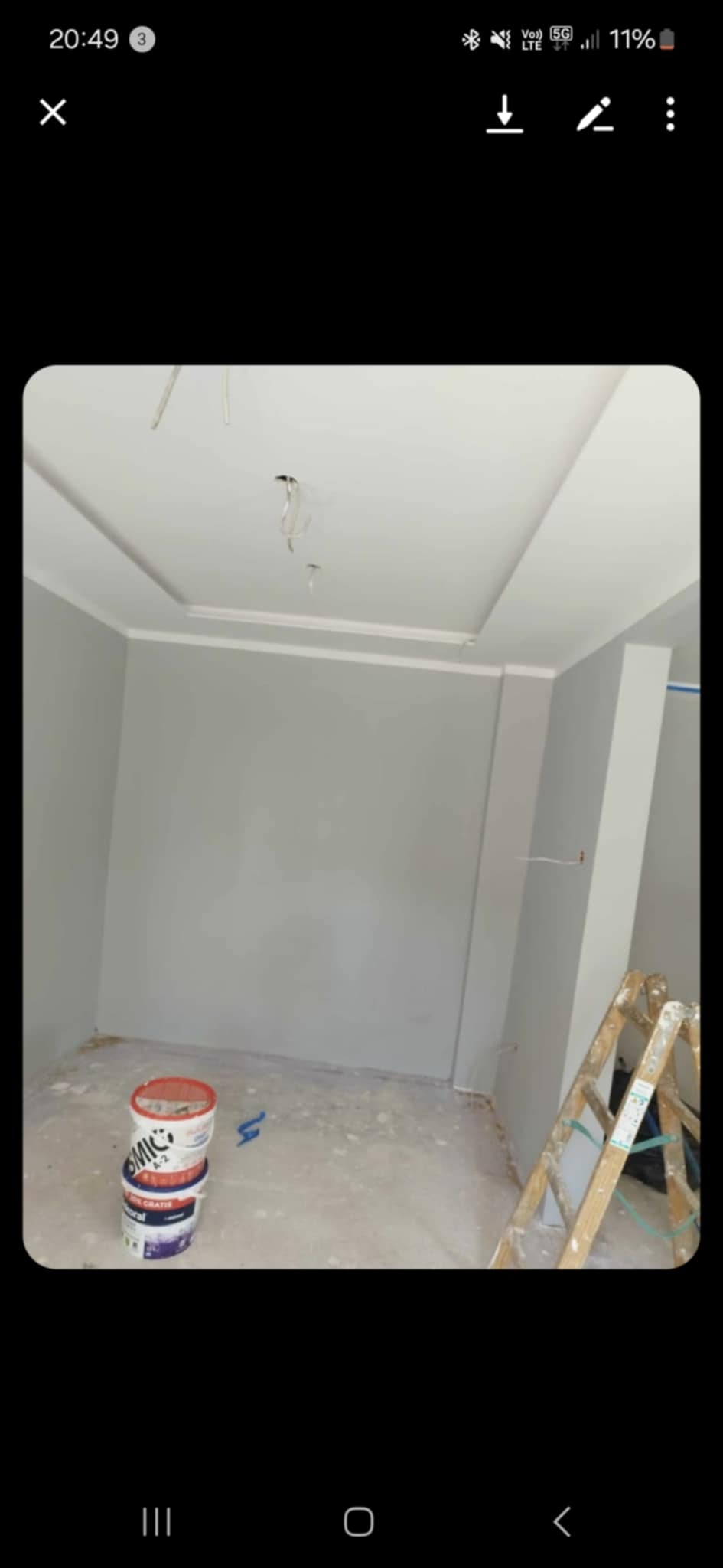 Pokój po malowaniu na szaro, widoczne puszki z farbą i drabina. Sufit podwieszany z listwami dekoracyjnymi.