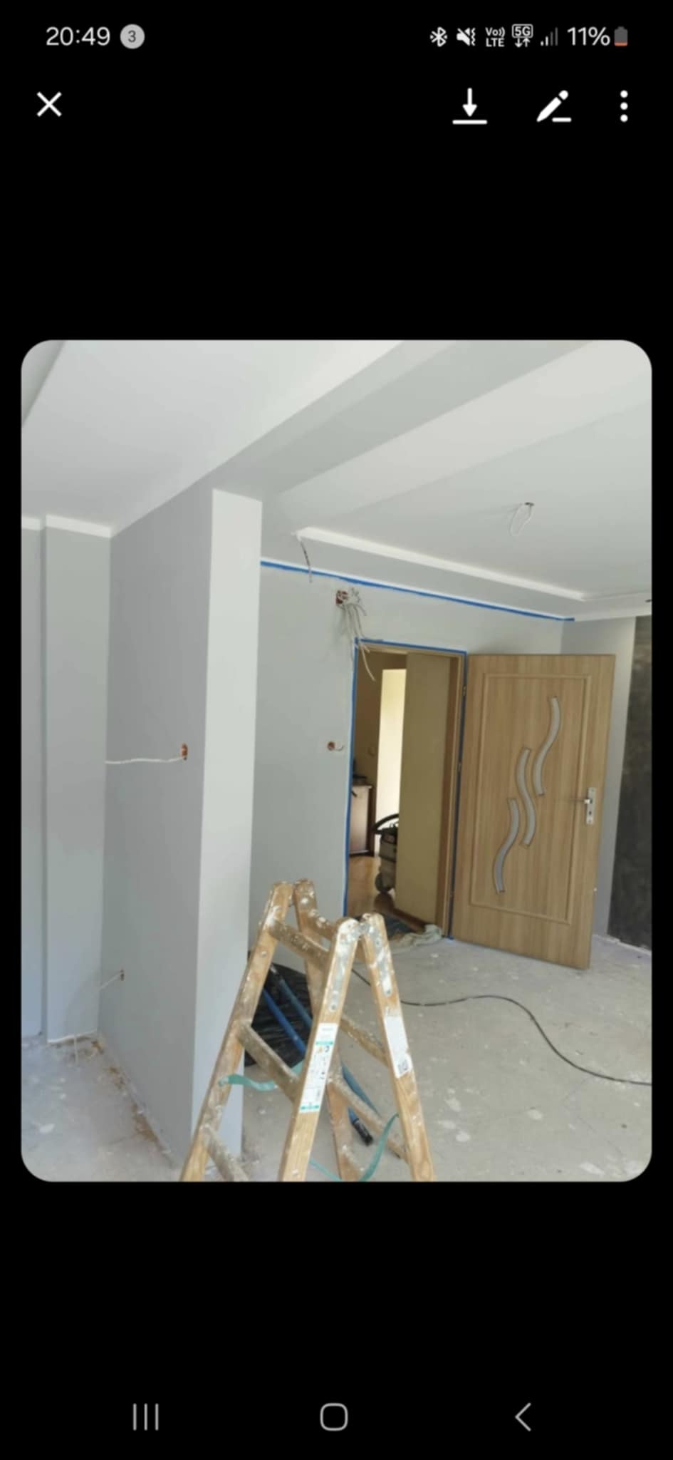 Świeżo pomalowane na szaro ściany w pomieszczeniu z drewnianą drabiną i częściowo widocznymi przewodami. Widoczne drzwi wewnętrzne z dekoracyjnym szkłem.