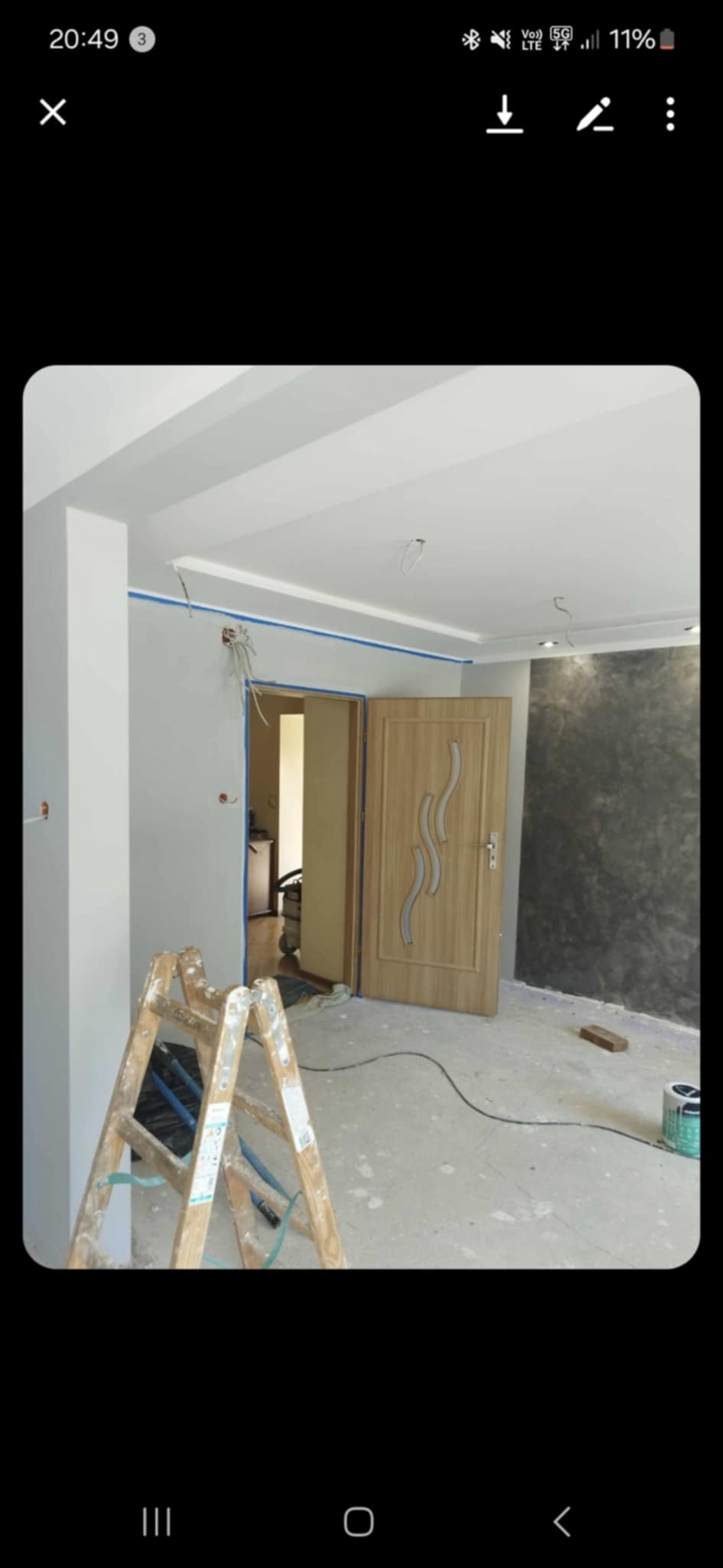 Wnętrze w trakcie malowania: drabina, ściany z taśmą malarską, częściowo pomalowana ściana dekoracyjna, otwarte drzwi. Widoczne kable i puszki elektryczne.
