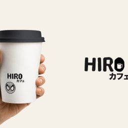 Pixeloza Studio - Dłoń trzyma biały kubek z czarnym wieczkiem, na którym widnieje logo 'HIRO カフェ' z symbolem Spider-Mana, obok widoczne większe logo 'HIRO' z ikoną filiżanki kawy. Minimalistyczny projekt graficzny.