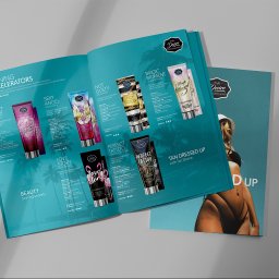 Pixeloza Studio - Otwarty katalog reklamowy z kosmetykami do opalania Tan Desire, prezentujący różne produkty z serii i ich składniki, obok leży zamknięty katalog z wizerunkiem opalonej modelki.