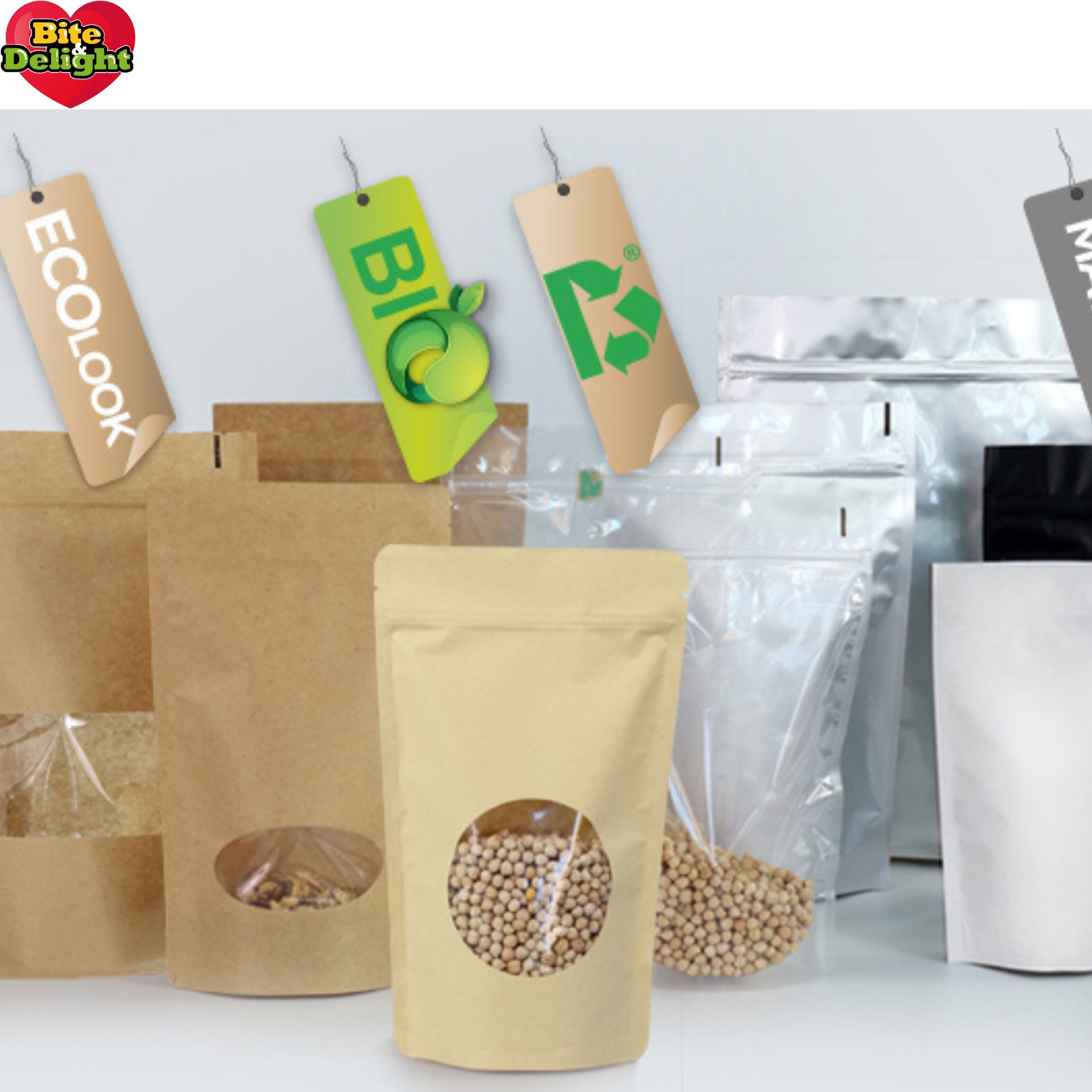 Różne rodzaje opakowań stojących, w tym papierowe z okienkiem wypełnione ziarnami, przezroczyste i metalizowane, z etykietami 'Ecolook', 'Bio' i symbolem recyklingu.