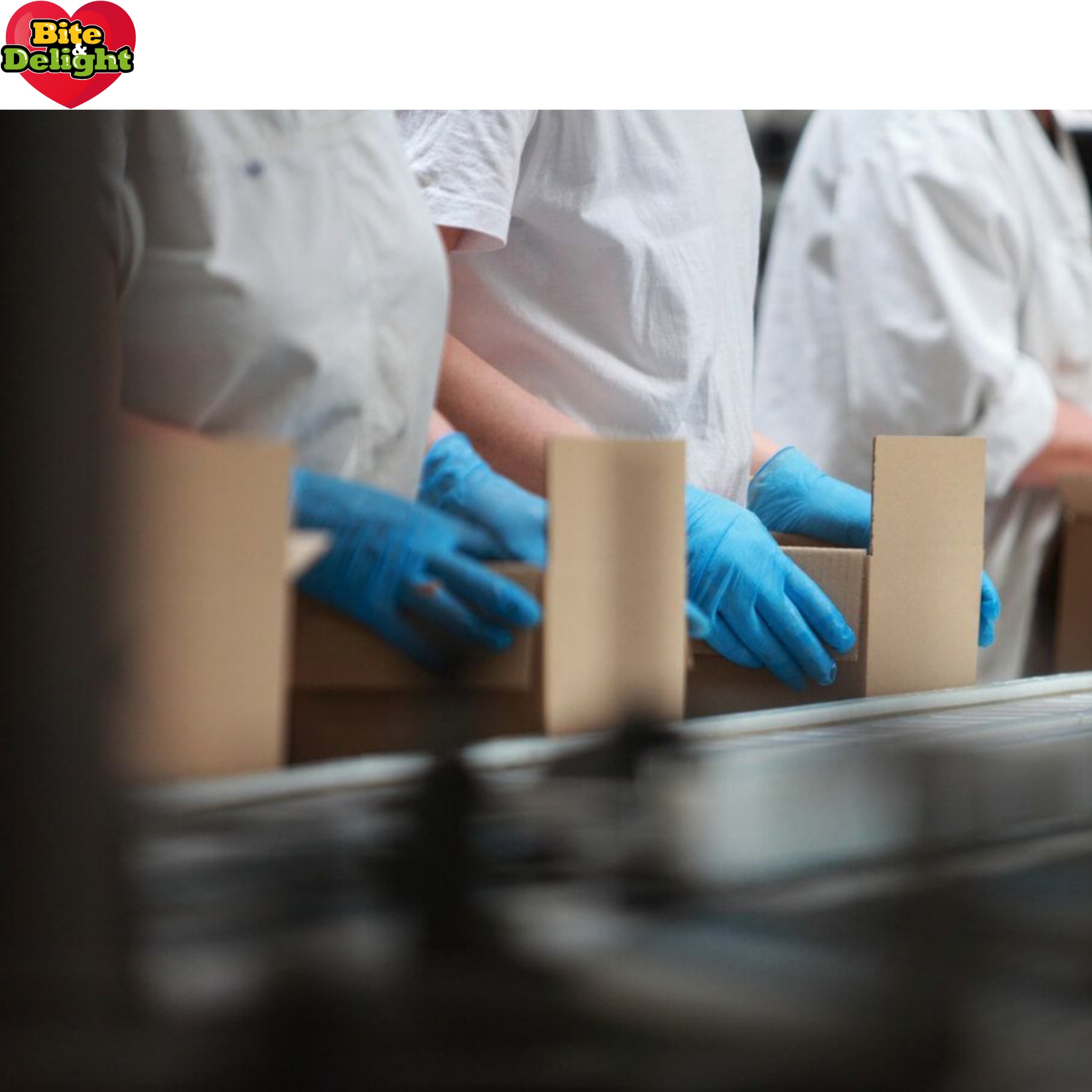 Pracownicy w białych uniformach i niebieskich rękawicach umieszczają kartonowe pudełka na linii produkcyjnej.