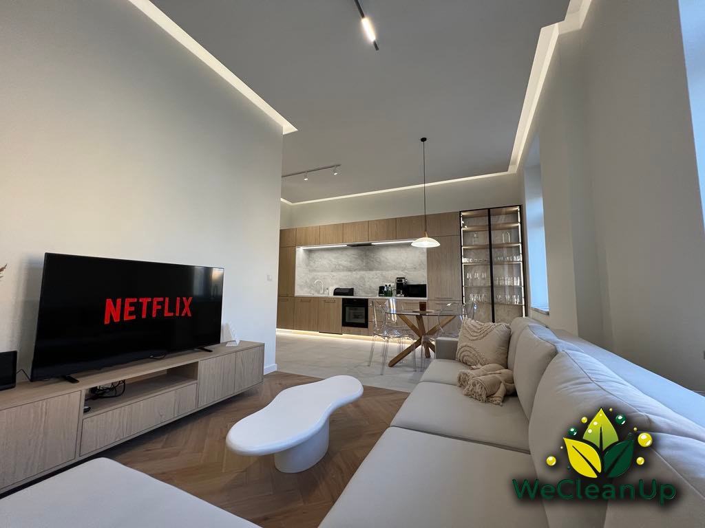 Jasne, przestronne wnętrze mieszkania z widocznym salonem, kuchnią i jadalnią, świeżo posprzątane, z logo WeCleanUp w prawym dolnym rogu.