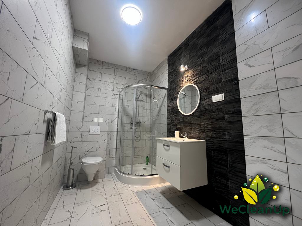 Nowoczesna, czysta łazienka z białymi marmurkowymi płytkami, czarną ścianą z kamienia dekoracyjnego, kabiną prysznicową i białą szafką pod umywalką, oświetlona światłem sufitowym i lampką...