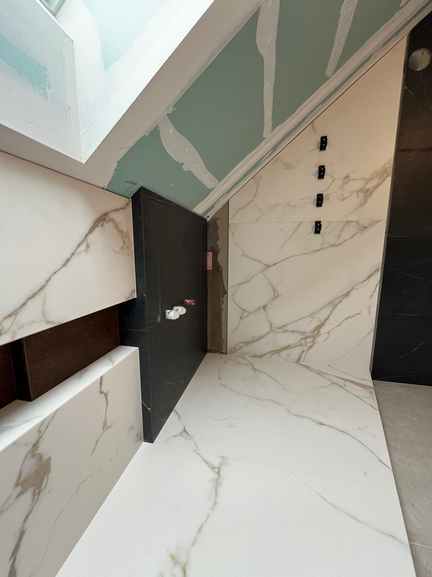 Ukończona łazienka z białymi płytkami imitującymi marmur i czarnymi akcentami. Widoczne fragmenty sufitu z płyt karton-gips. Nowoczesny design.