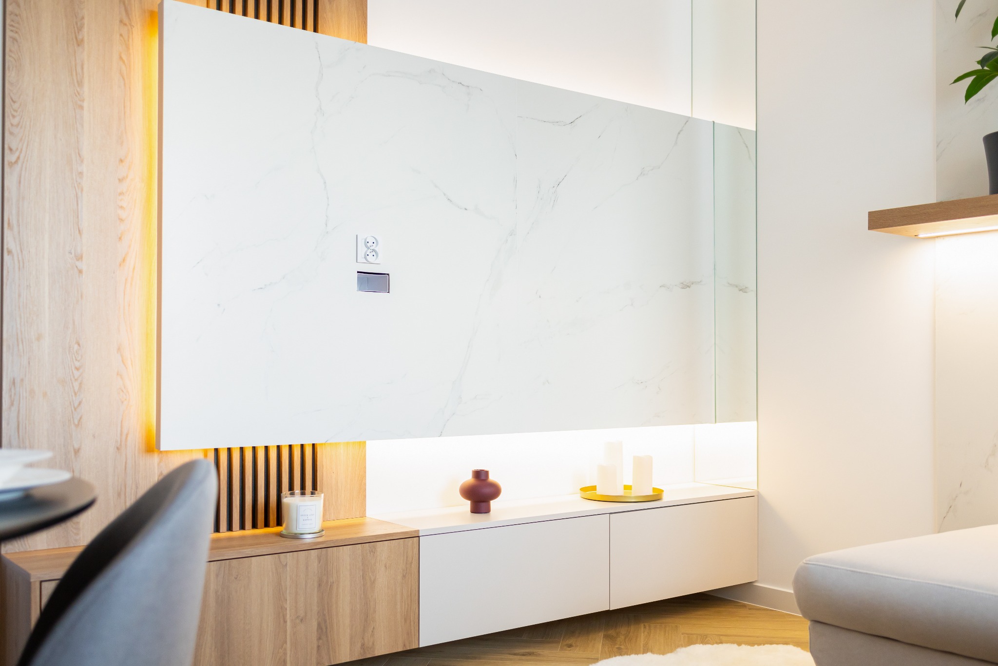 Nowoczesna ściana TV z białym marmurem, podświetleniem LED i drewnianymi akcentami. Minimalistyczny design z gniazdami elektrycznymi i dekoracjami.