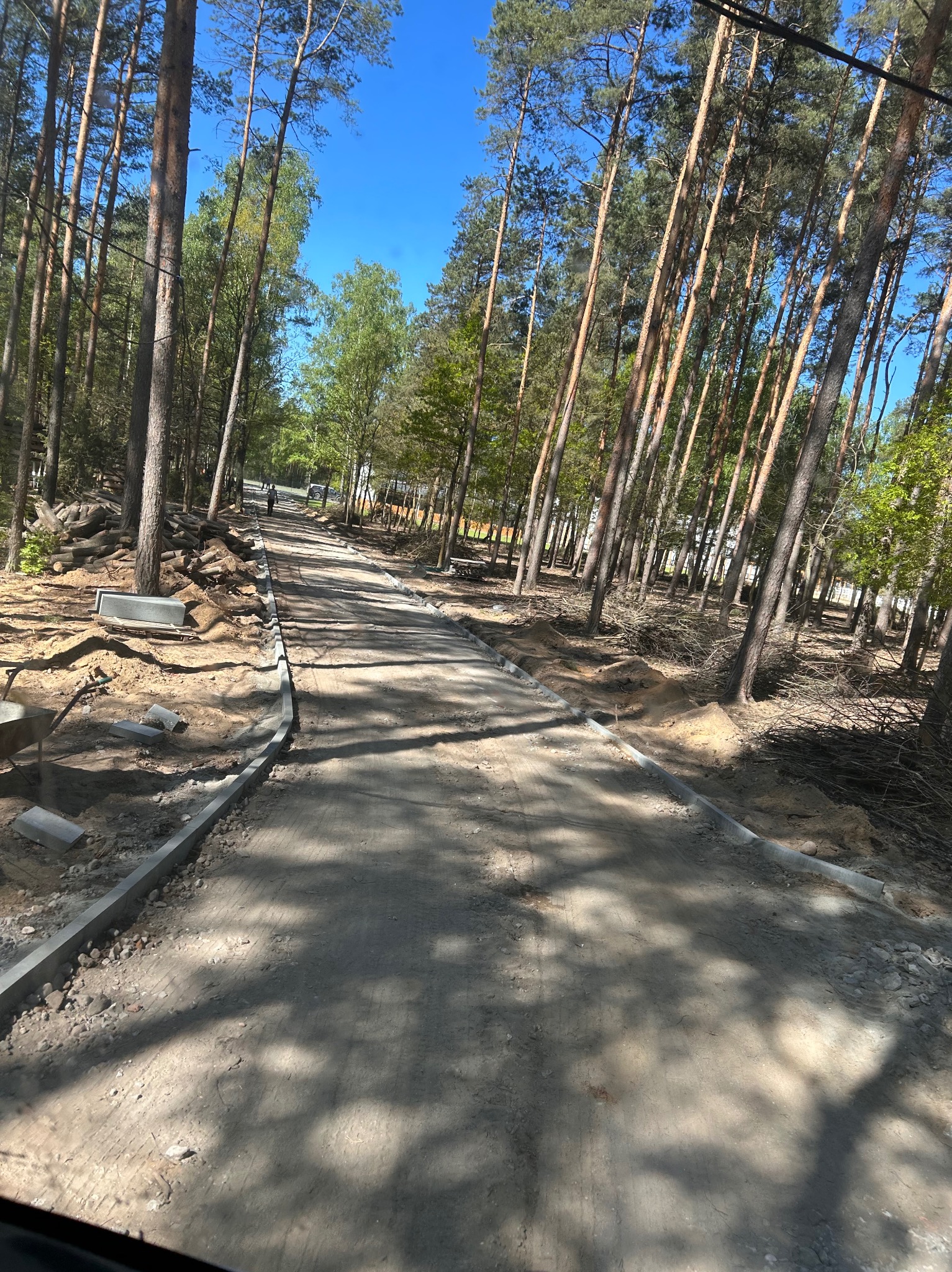 Budowa drogi leśnej: widok na ułożone obrzeża betonowe, przygotowany grunt, drzewa po bokach. Etap prac przed utwardzeniem nawierzchni.