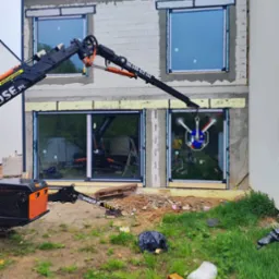 Montaż okna z użyciem dźwigu przyssawkowego na budowie domu. Widoczne okna na różnych etapach instalacji, ściany z betonu komórkowego.