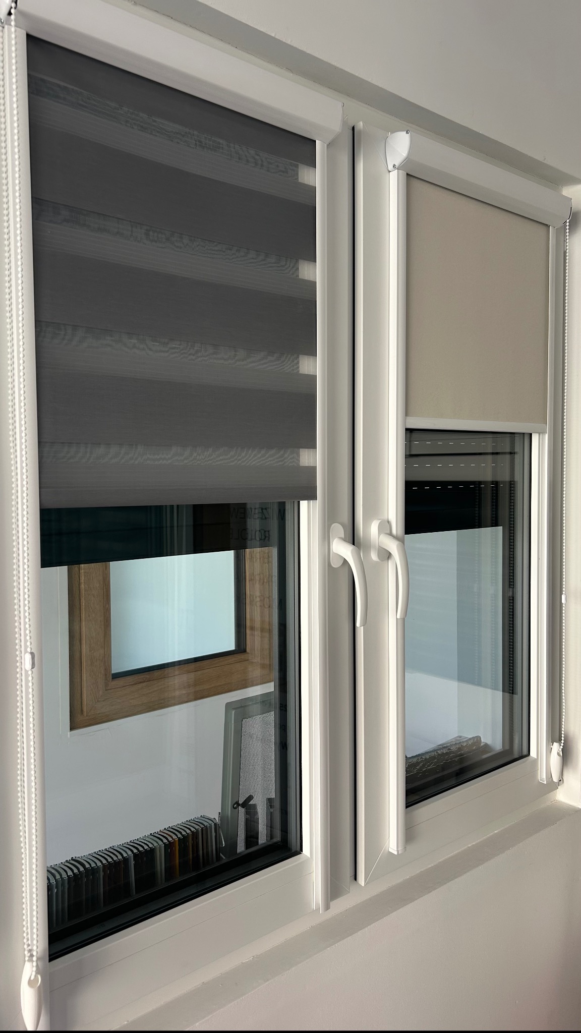 Białe okno PCV z zamontowanymi roletami dzień i noc w kolorze szarym i beżowym, widok z bliska na mechanizm łańcuszkowy.