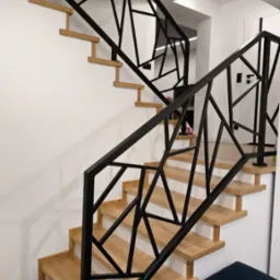 Schody drewniane z czarną, geometryczną balustradą metalową, widoczne z boku, z fragmentem niebieskiej pufy w dolnym rogu.