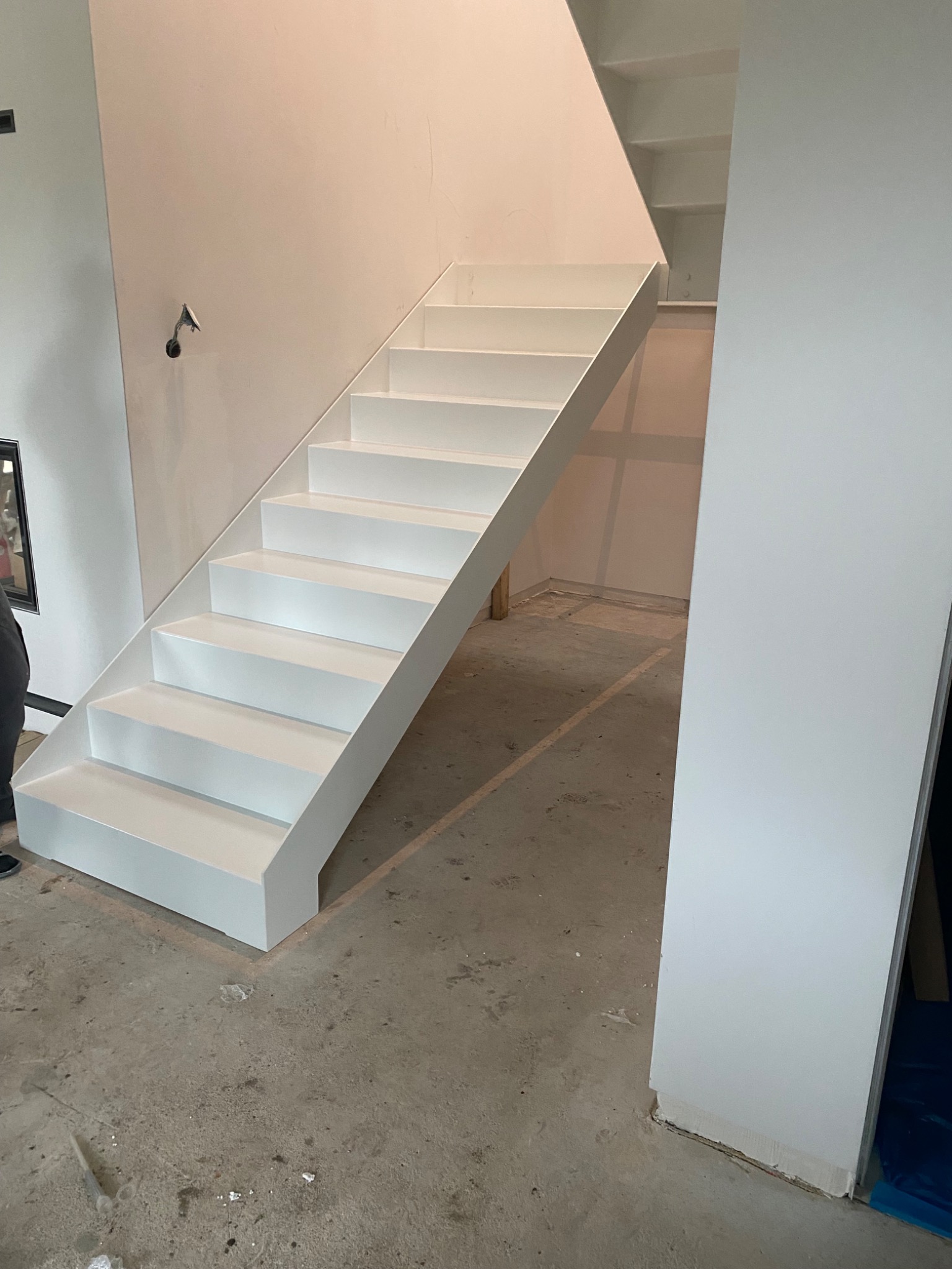 Surowe, białe schody metalowe bez poręczy, w trakcie montażu w nowym budynku, z widocznymi elementami konstrukcyjnymi i surowym betonem na podłodze.