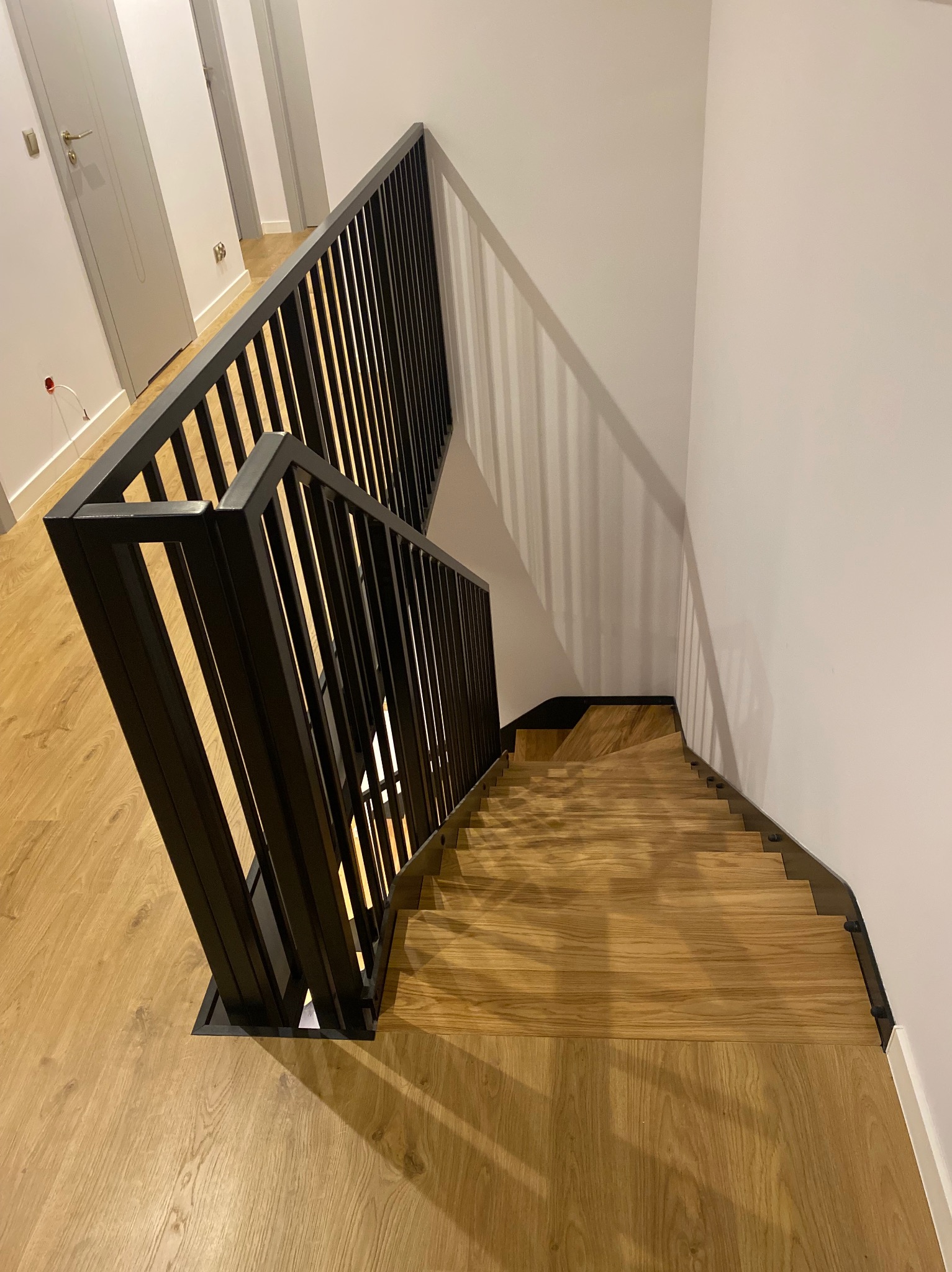 Nowoczesne schody z drewnianymi stopniami i czarną metalową balustradą, widok z góry, minimalistyczny design.