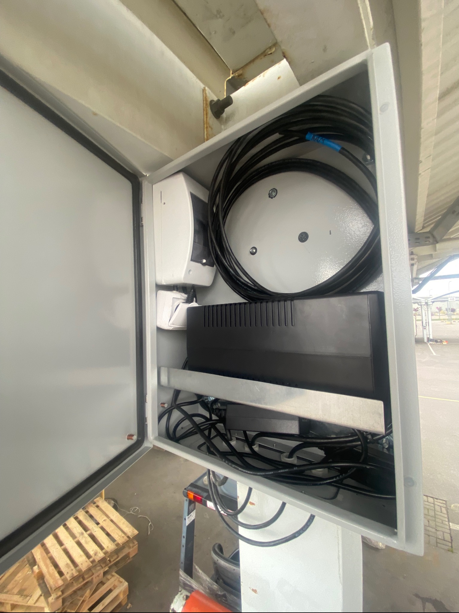 Otwarta szara szafa sterownicza z widocznymi elementami instalacji elektrycznej, w tym przewody, listwa zaciskowa i zasilacz impulsowy, zamontowana pod metalową konstrukcją.