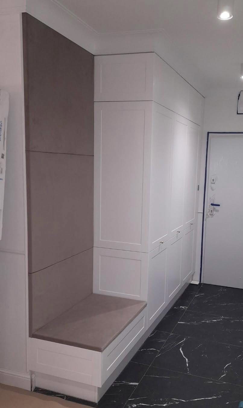 Biała zabudowa w przedpokoju z siedziskiem i panelami ściennymi w odcieniach szarości.  Eleganckie wykończenie, marmurowe płytki podłogowe.