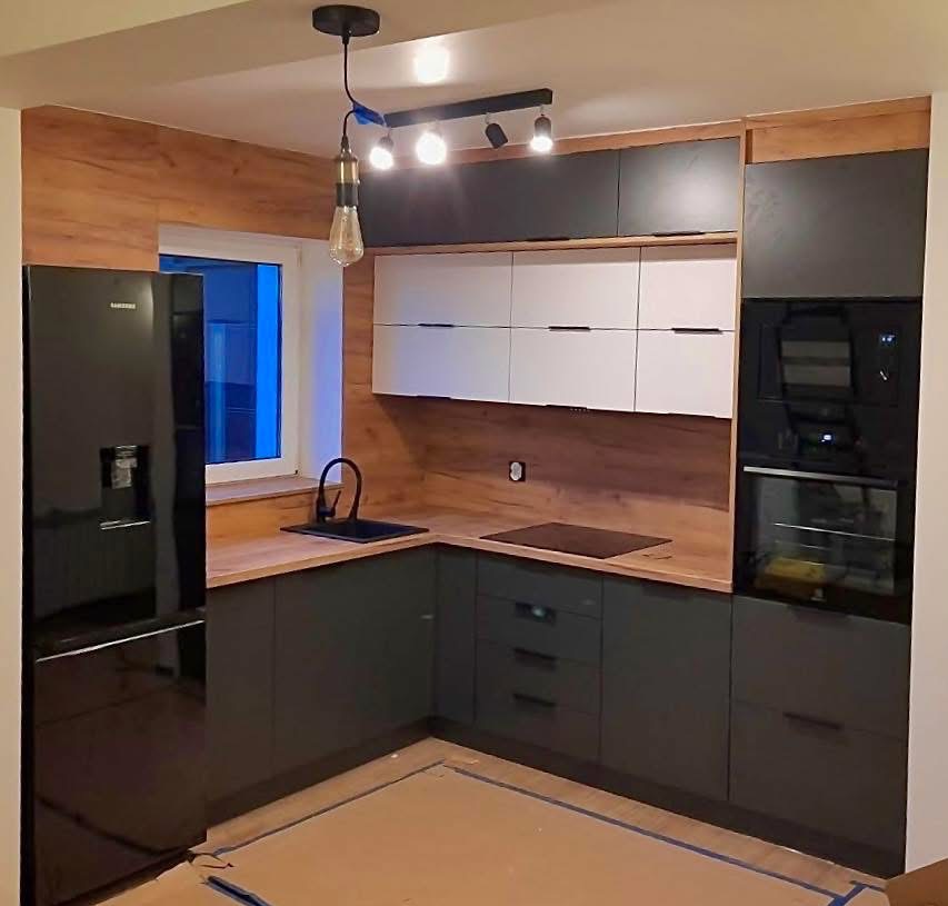 Nowoczesna kuchnia w odcieniach szarości i drewna z czarnym sprzętem AGD. Uwagę przykuwa designerska lampa wisząca nad zlewem i minimalistyczne oświetlenie podszafkowe.