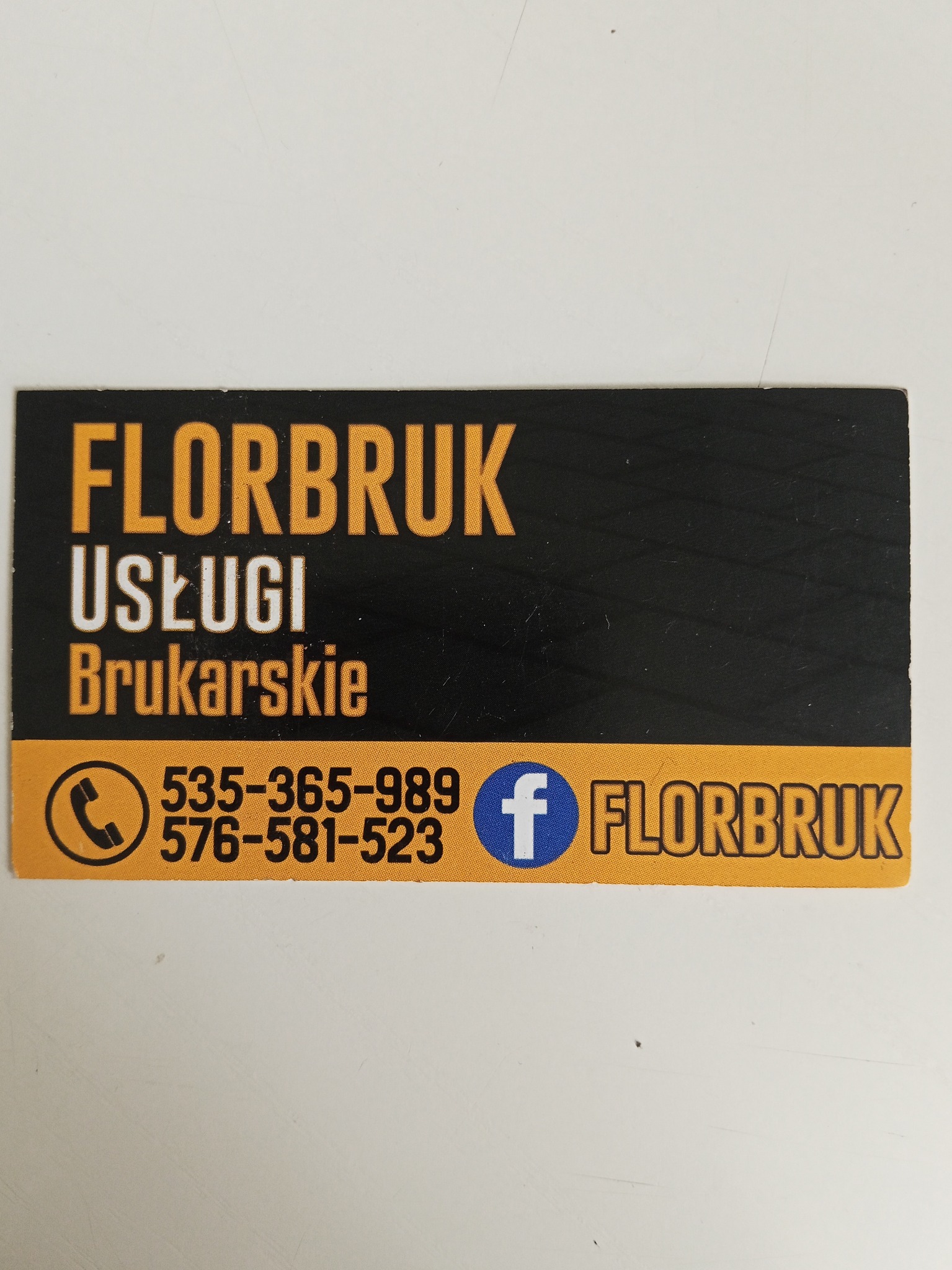Wizytówka firmy FLBRUK oferującej usługi brukarskie. Na czarnym tle widnieje napis 'FLORBRUK Usługi Brukarskie' oraz numery telefonów i ikona Facebooka.