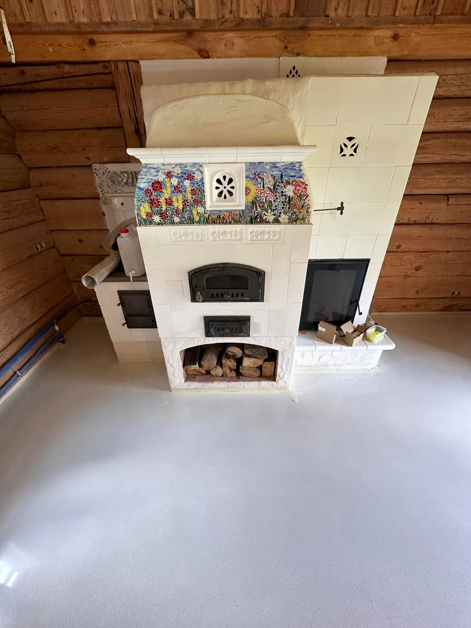 Jasnoszara, gładka podłoga w drewnianym domu z piecem kaflowym zdobionym kwiatowym motywem, prezentująca dekoracyjne wykończenie podłogowe.