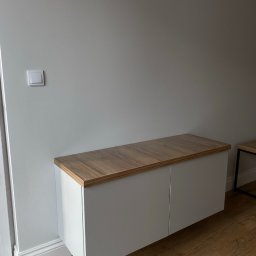 Volodymyr Khomliak - Biała szafka wisząca z blatem w kolorze drewna, zamontowana pod ścianą z włącznikiem światła, widoczna na tle drewnianej podłogi.