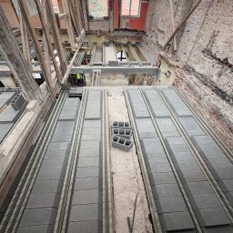 RENEWAL CONSTRUCTIONS SPÓŁKA Z OGRANICZONĄ ODPOWIEDZIALNOŚCIĄ - Wnętrze remontowanego budynku z widocznymi bloczkami betonowymi ułożonymi w rzędach, drewnianą konstrukcją dachu i fragmentami odsłoniętej cegły na ścianach.