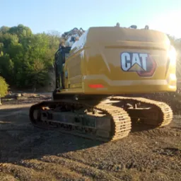 Żółta koparka gąsienicowa marki CAT na placu budowy z widocznym logo, w tle drzewa i błękitne niebo.