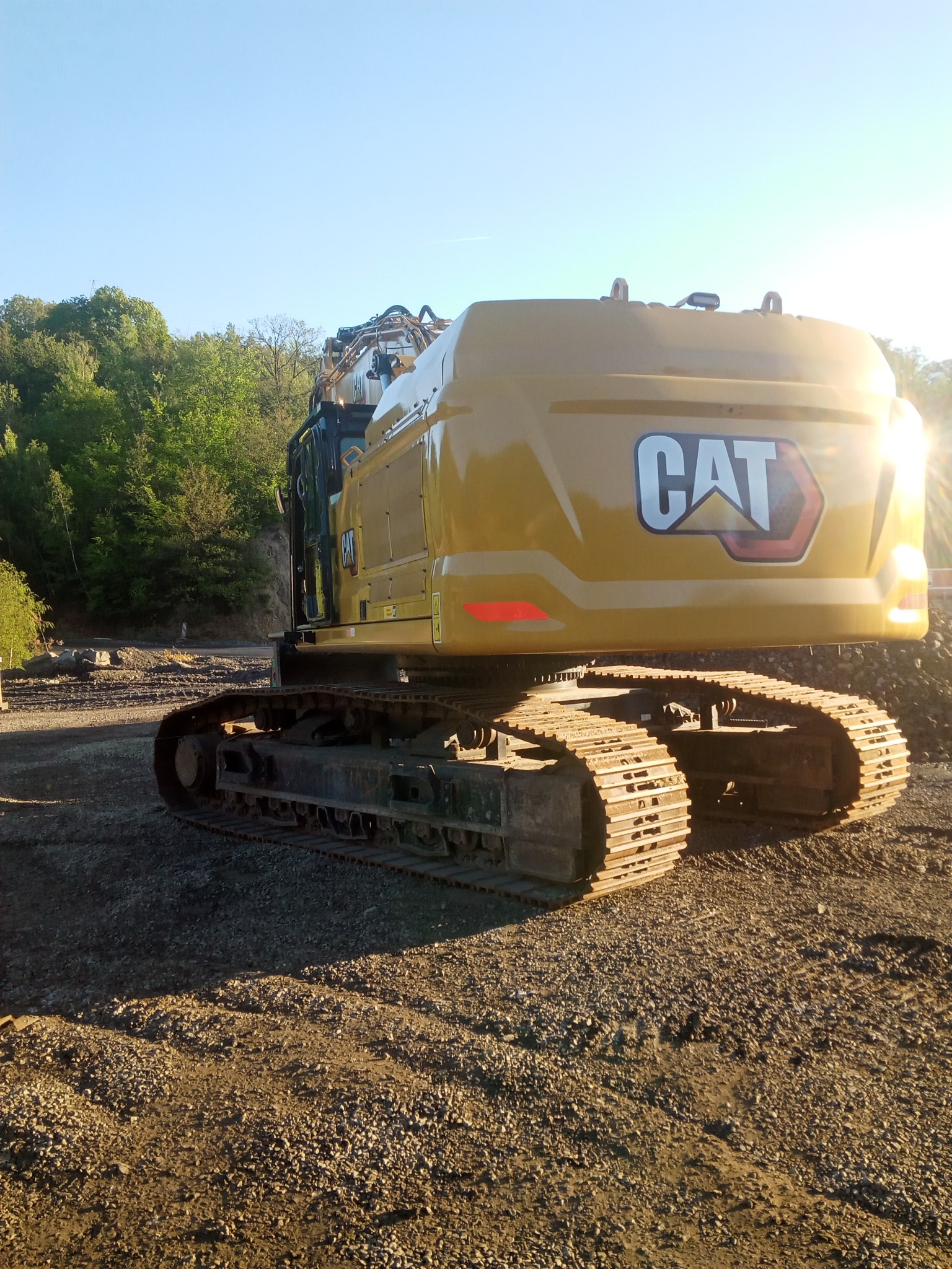 Żółta koparka gąsienicowa marki CAT na placu budowy z widocznym logo, w tle drzewa i błękitne niebo.