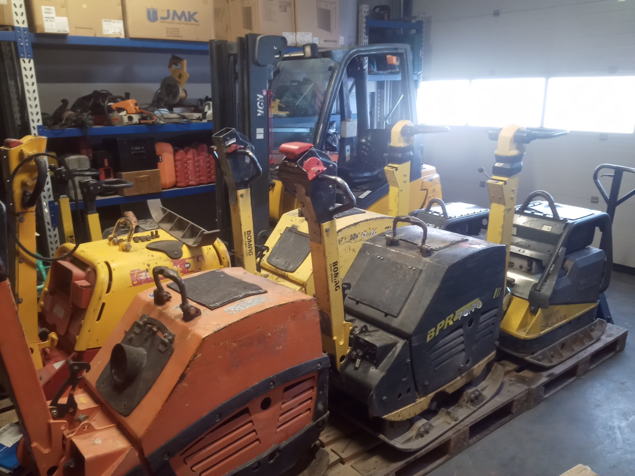 Magazyn w Łodygowicach z zagęszczarkami płytowymi różnych marek (Bomag, Wacker Neuson) i wózek widłowy w tle.