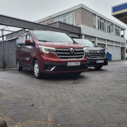 Twój-BUS - Dwa busy Renault Trafic zaparkowane przed myjnią samochodową, jeden bordowy z polską rejestracją, drugi ciemny z zagraniczną.