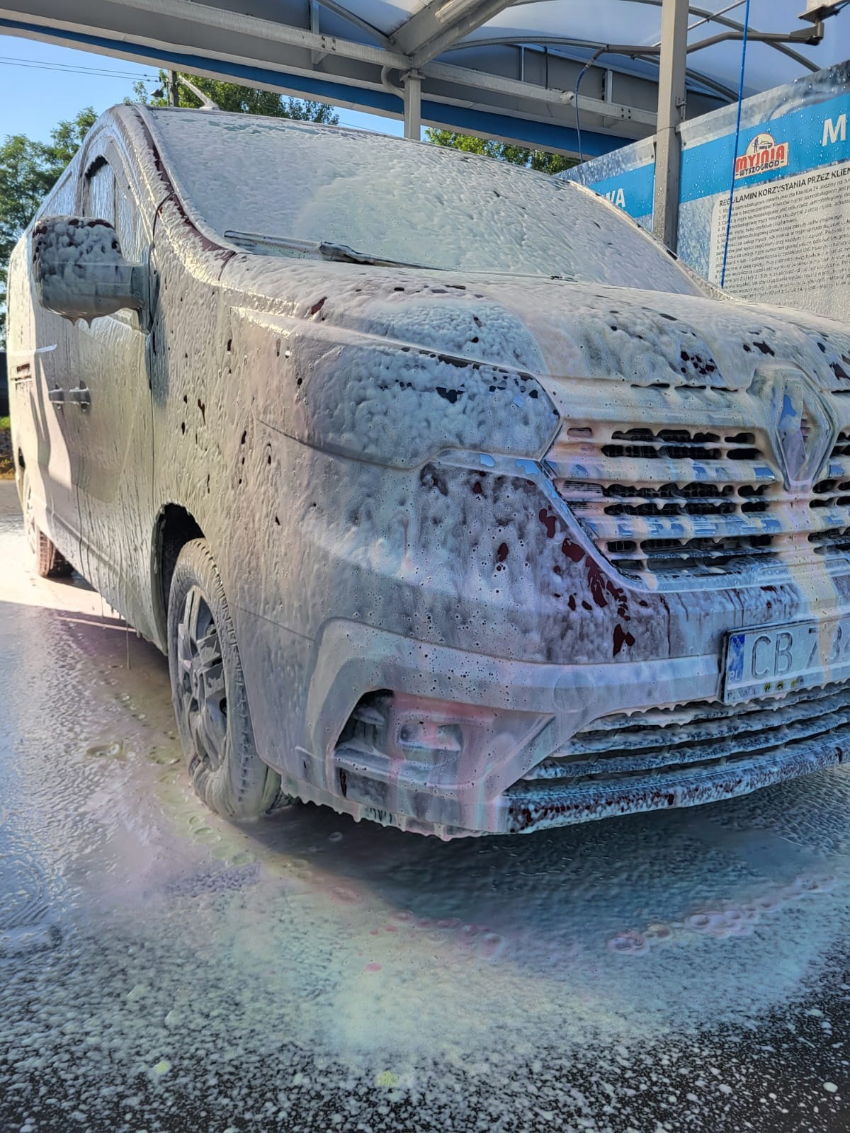 Czerwony van Renault pokryty grubą warstwą piany myjącej w myjni samochodowej.