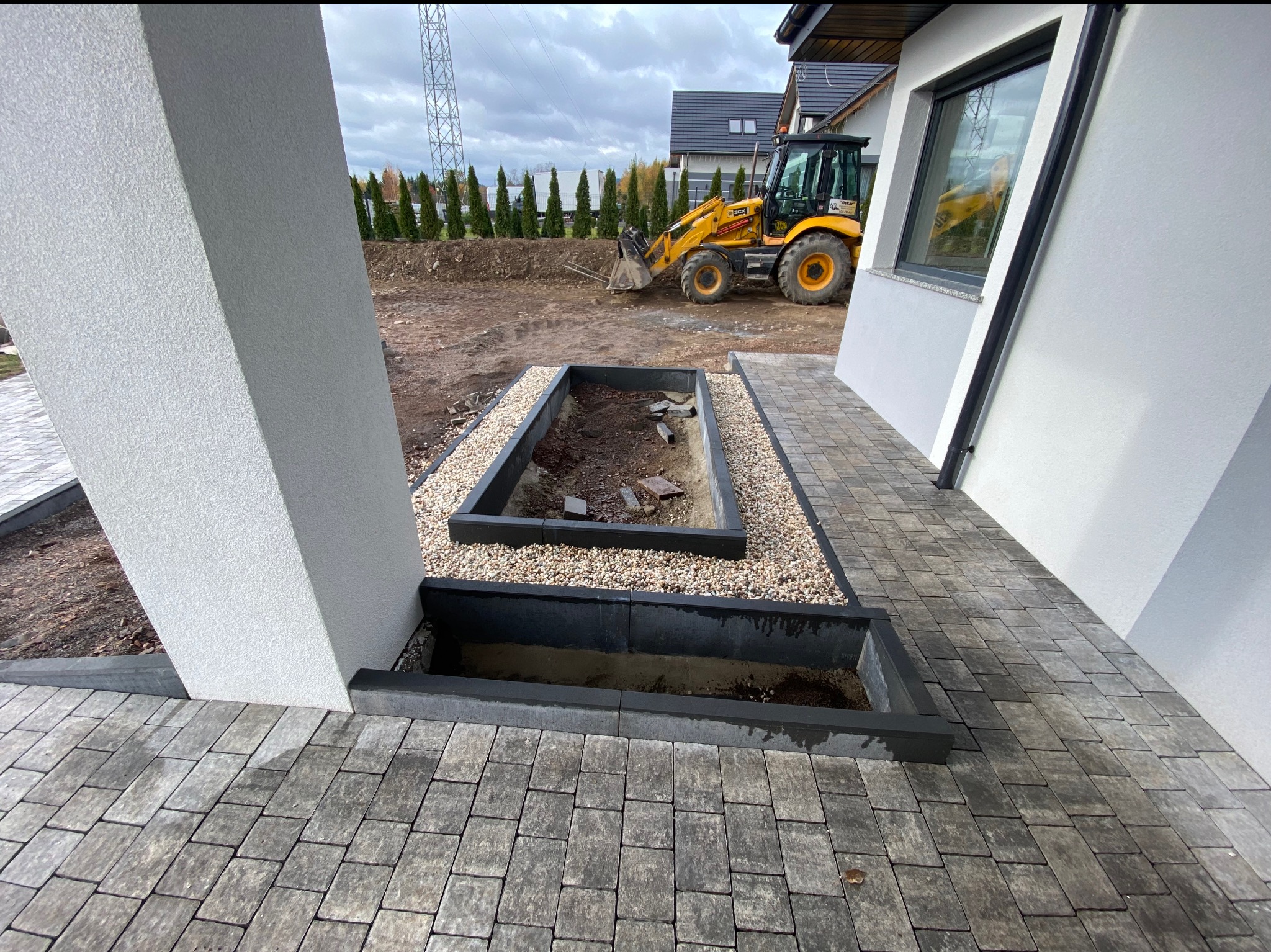 Przygotowanie terenu pod nasadzenia roślin w nowoczesnym ogrodzie, widoczny traktor oraz wyłożona kostka brukowa i obrzeża rabat.