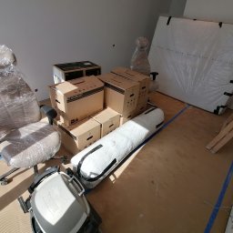 MATEUSZ JEŻEWSKI - Spakowane meble, krzesło biurowe owinięte folią, kartony Spaceo i materac przygotowane do transportu, widoczne zabezpieczenia podłogi taśmą