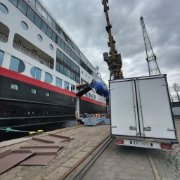 MATEUSZ JEŻEWSKI - Ciężarówka dostawcza z otwartymi drzwiami zaparkowana obok statku wycieczkowego w porcie w Straszynie, z dźwigiem w tle i pracownikami w kamizelkach odblaskowych biorącymi udział w załadunku.