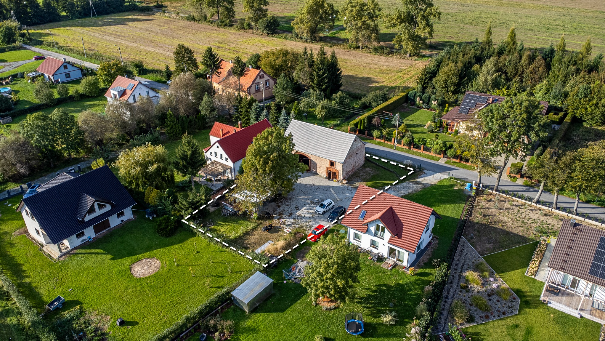 Działka z zabudowaniami w Krzyżowicach, widok z lotu ptaka. Granice działki wyznaczone białą linią. Na podwórku stoją samochody. Piękna okolica.